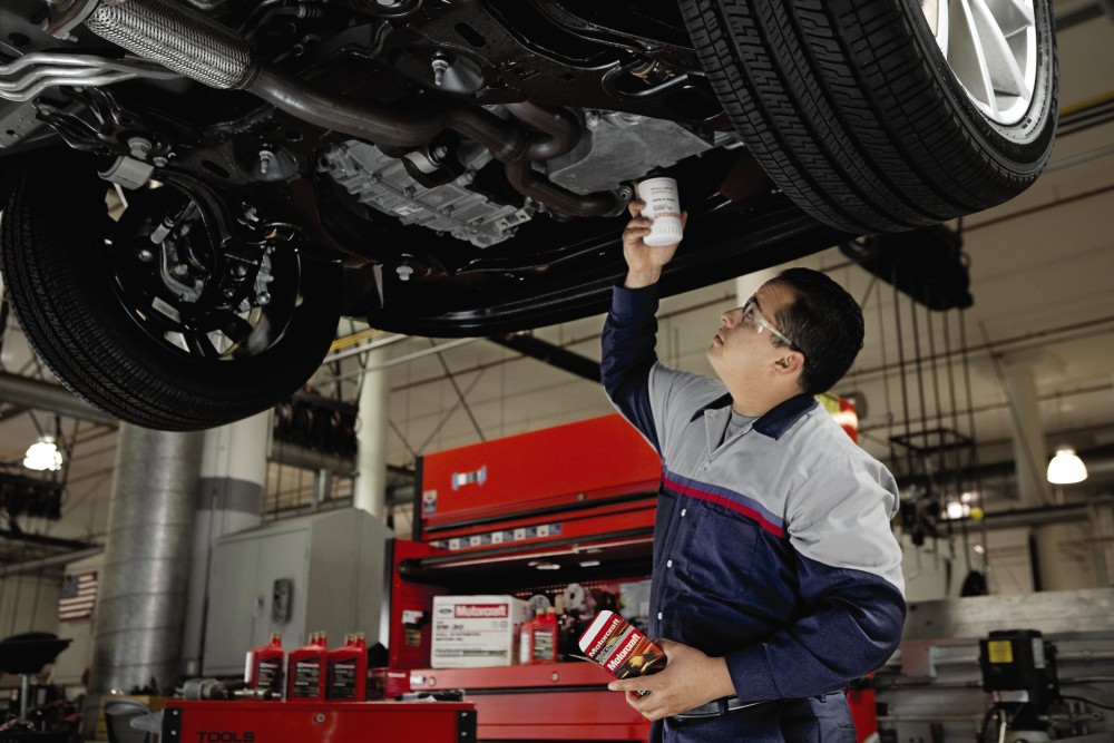 A mechanic replacing an oil filter under a raised vehicle in an auto repair shop.