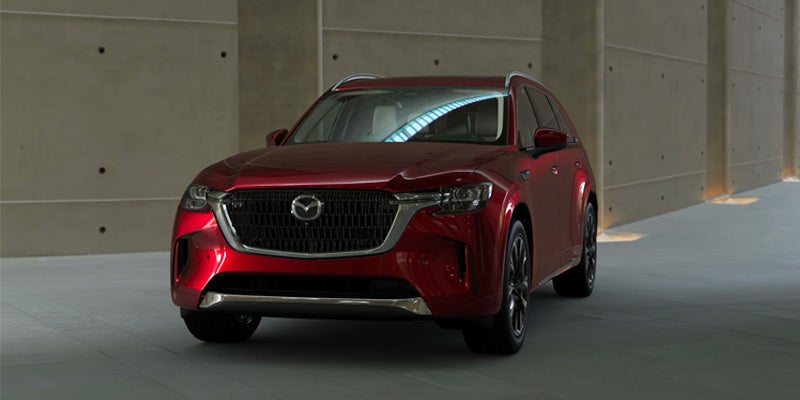 Front view of a shiny red Mazda CX-90 SUV parked in a garage with cement walls.