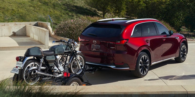 Rear view of a red SUV towing a vintage grey motorcycle on a trailer on a paved road.