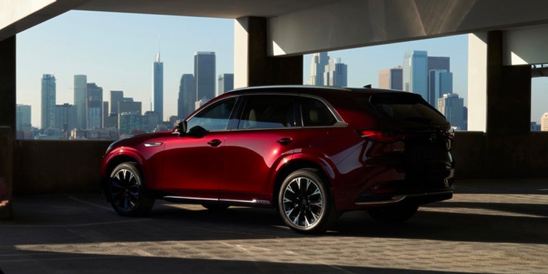 A red SUV is parked in a garage with a view of a city skyline at sunset.