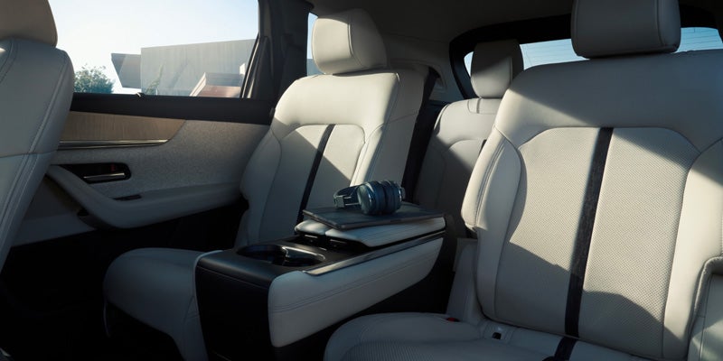 Inside a car, white leather captain's chairs with black accents. Headphones and a tablet rest on the console.