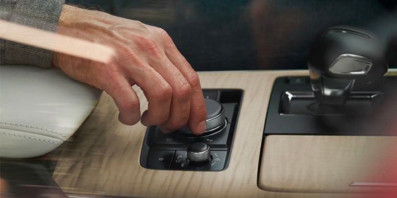 A person's hand adjusts a rotary dial on the center console of a car, which has a wood-grain finish.