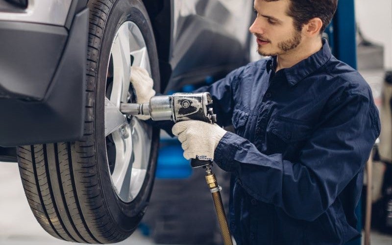 Auto technician using an impact wrench to service a vehicle tire.